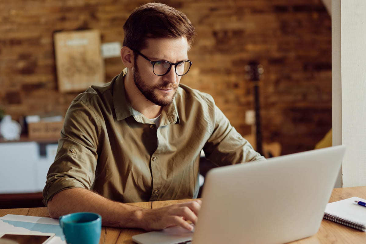 Homem trabalhando em home office com notebook sobre mesa de madeira