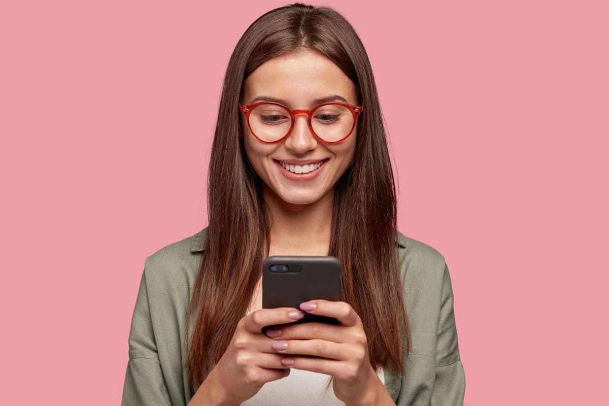 Mulher Usando Facebook Messenger Ads em celular com fundo rosa na imagem