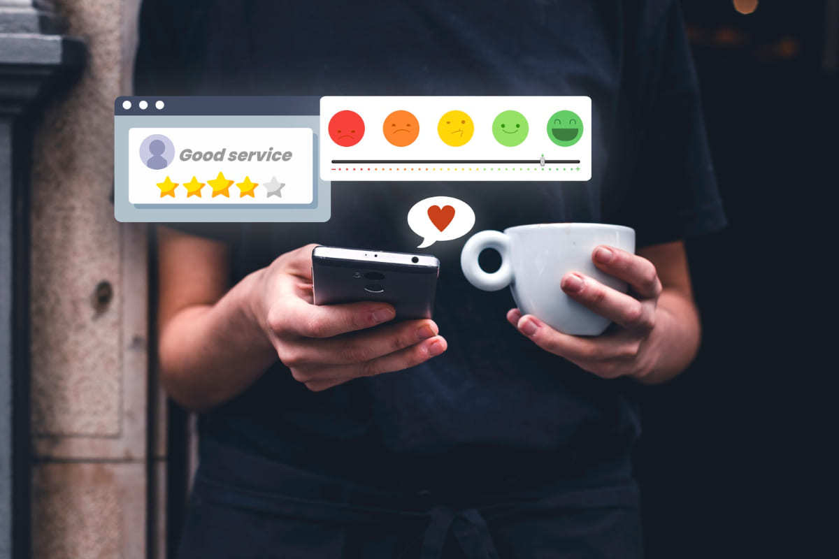 Pessoa usando smartphone enquanto segura xícara grande na cor branca com símbolos web de avaliação de serviços e de coração das redes sociais à sua frente e como se saíssem da tela do celular