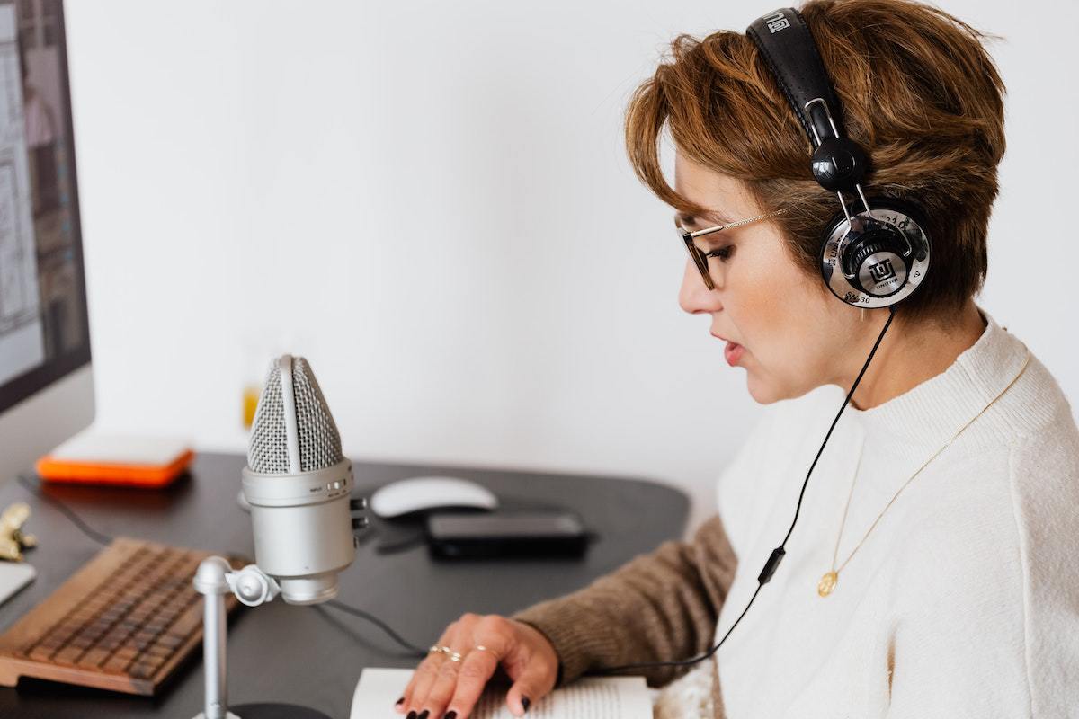 Mulher sentada diante de mesa escura com computador e microfone enquanto faz gravação de áudio para melhoria com Adobe audition
