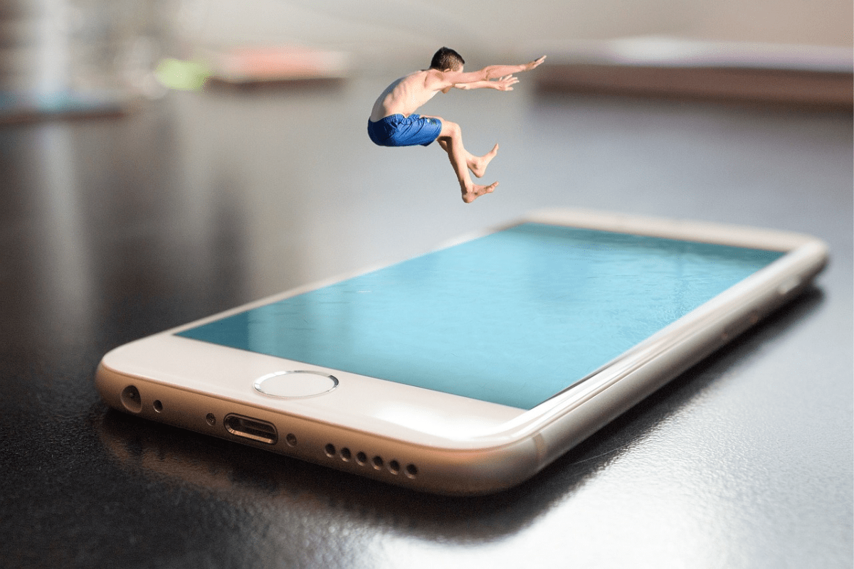 Montagem de homem mergulhando em tela de aparelho celular sobre mesa escura com objetos de escritório em desfoco ao fundo após edição de imagem