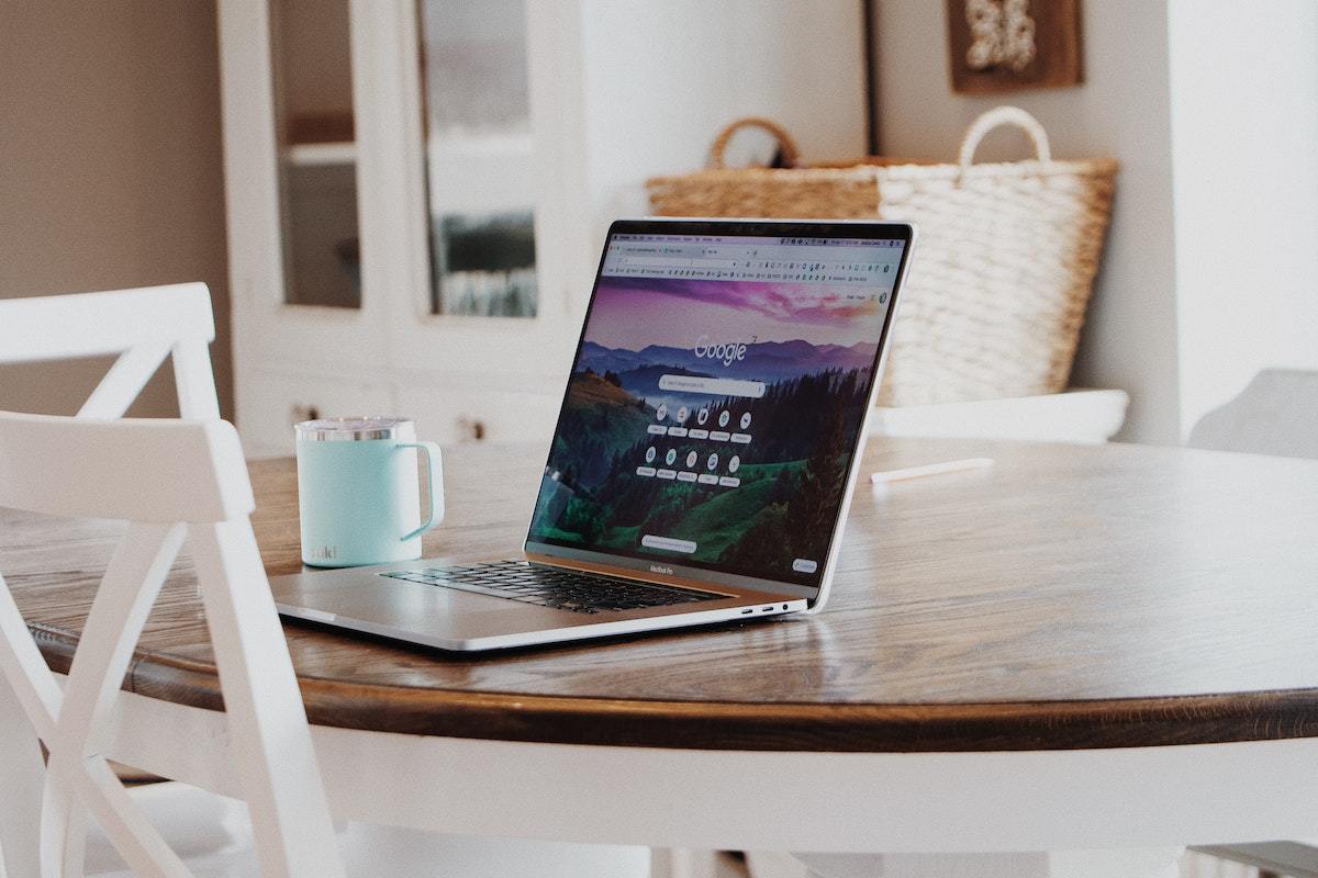 Notebook sobre mesa de madeira redonda em cozinha de casa com tela inicial do Google aberta