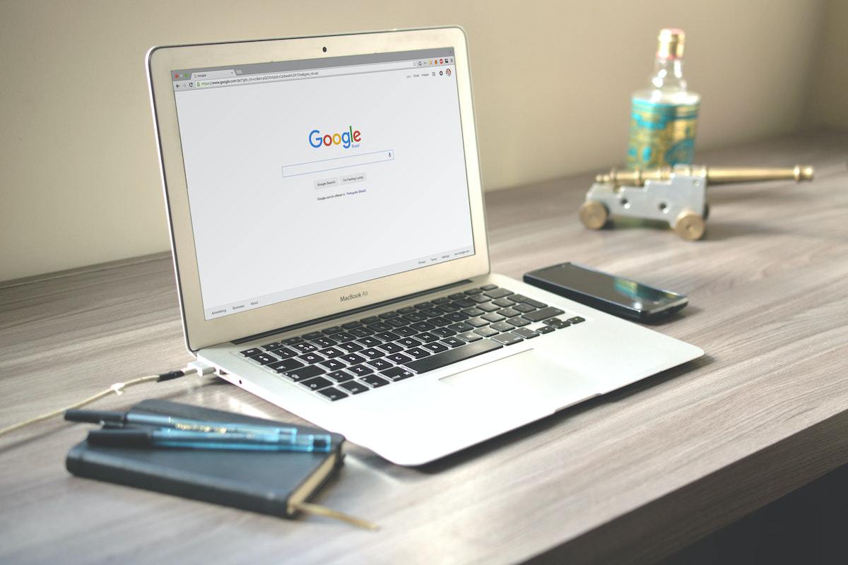 Notebook com tela inicial de Pesquisa do maior motor de buscas com agenda, celular e caneta ao seu redor para Anunciar no Google