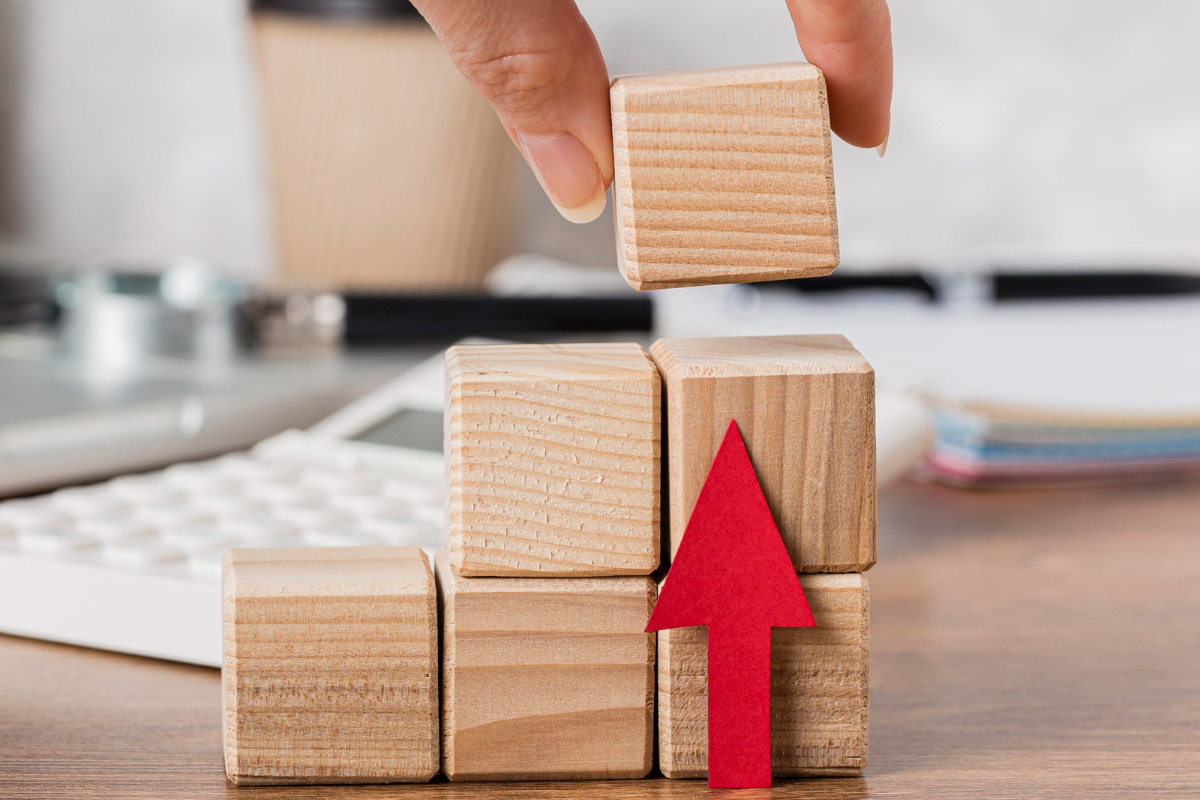 Lucro: CAC de SaaS Pessoa fazendo pilha com blocos de madeira e seta vermelha apontando pra cima sobre mesa de madeira simbolizando lucro