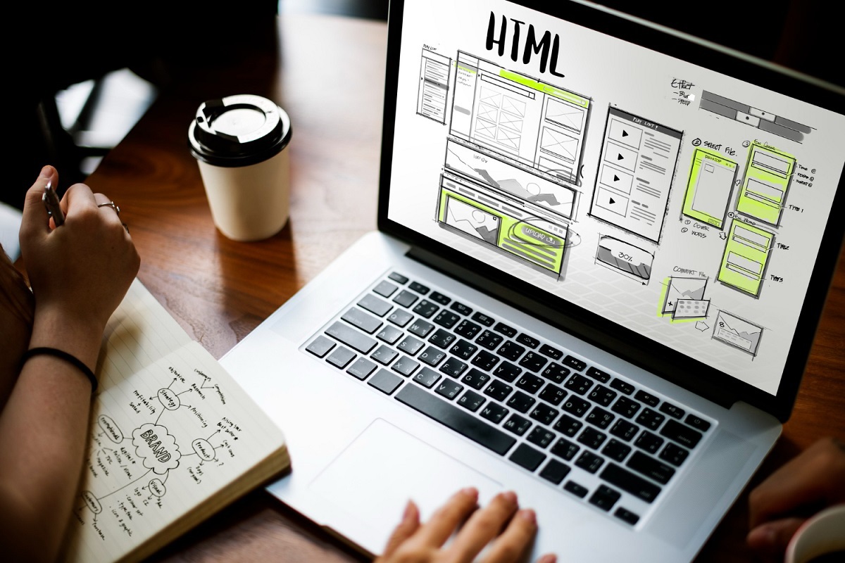 CMS e Hospedagem representados por duas pessoas usando notebook sobre mesa de madeira com sua tela exibindo montagem com gráficos e fluxograma além de nome HTML acima de tudo