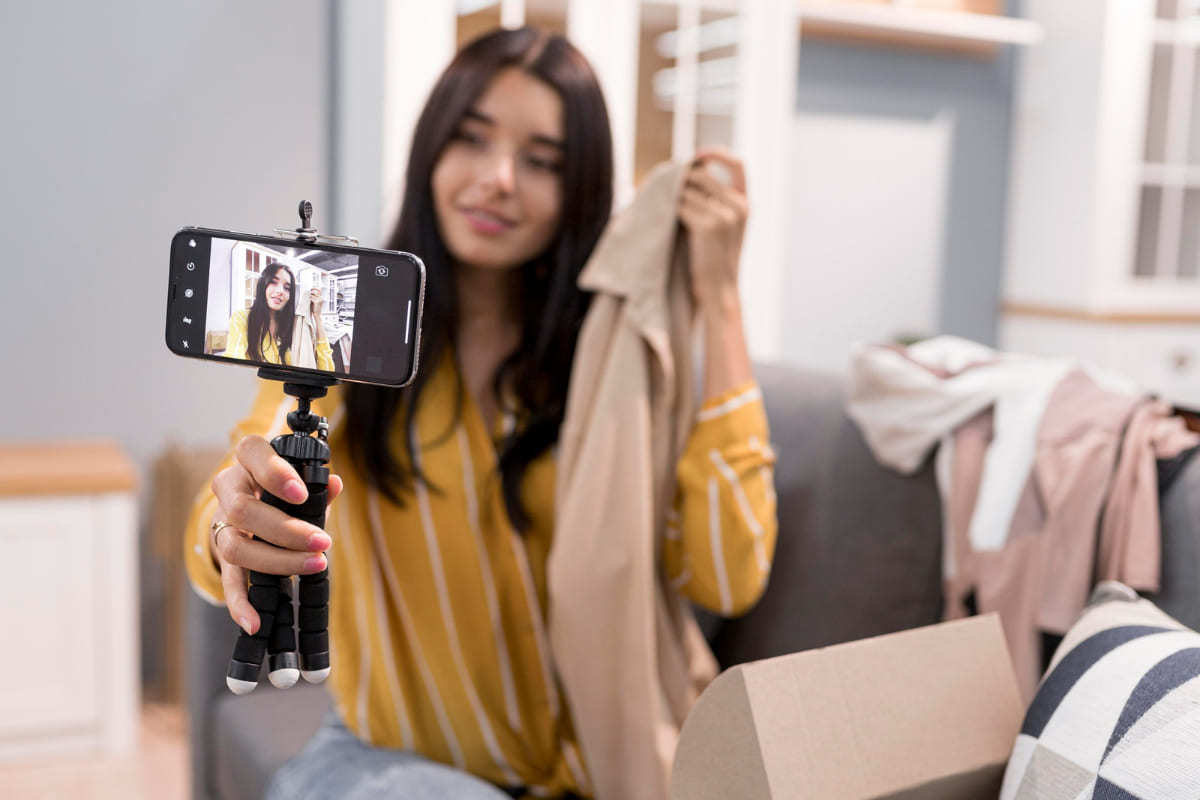 Mulher gravando vídeo com celular em pedestal mostrando roupas