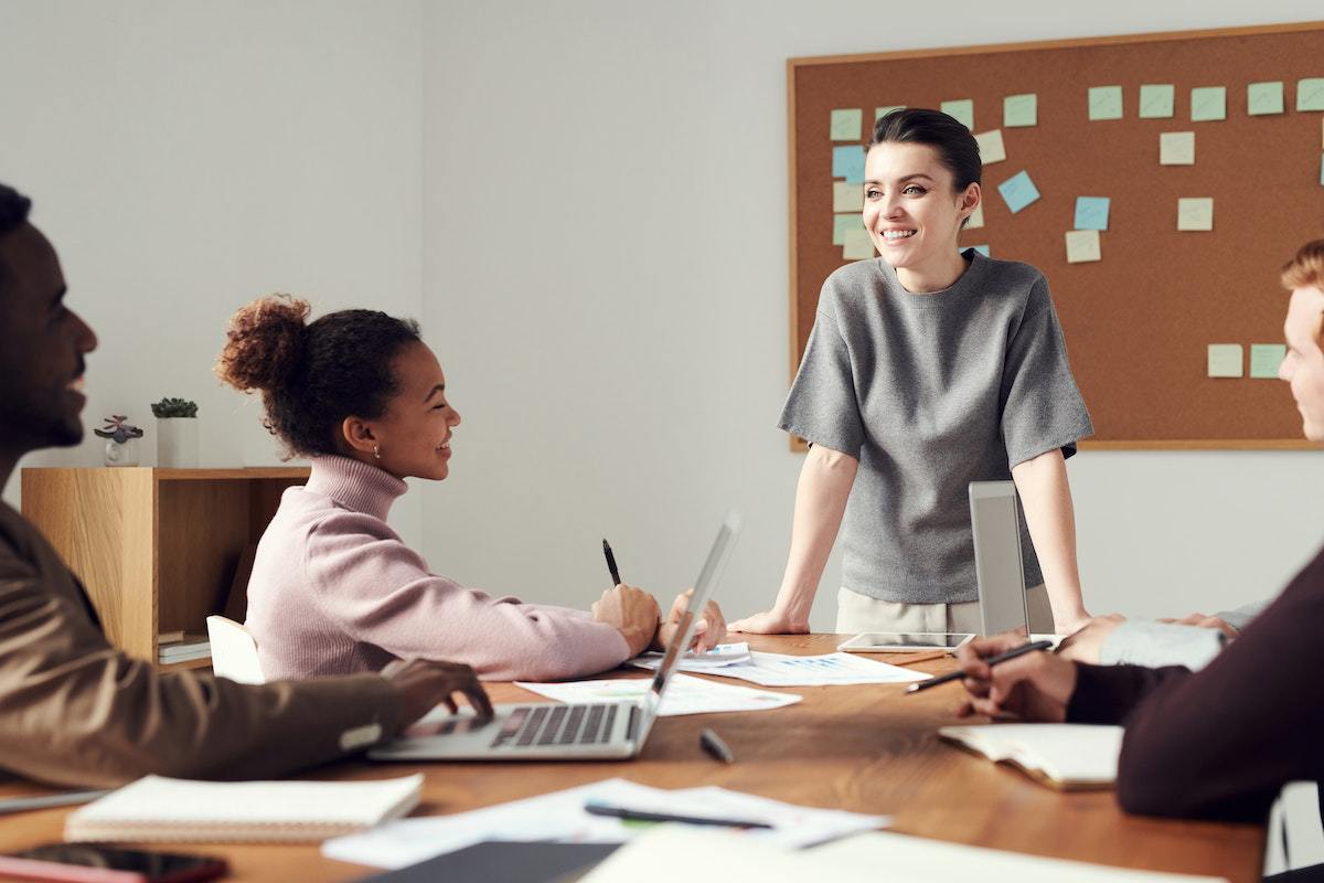 Mulher de pé liderando reunião com equipe sentada à sua frente