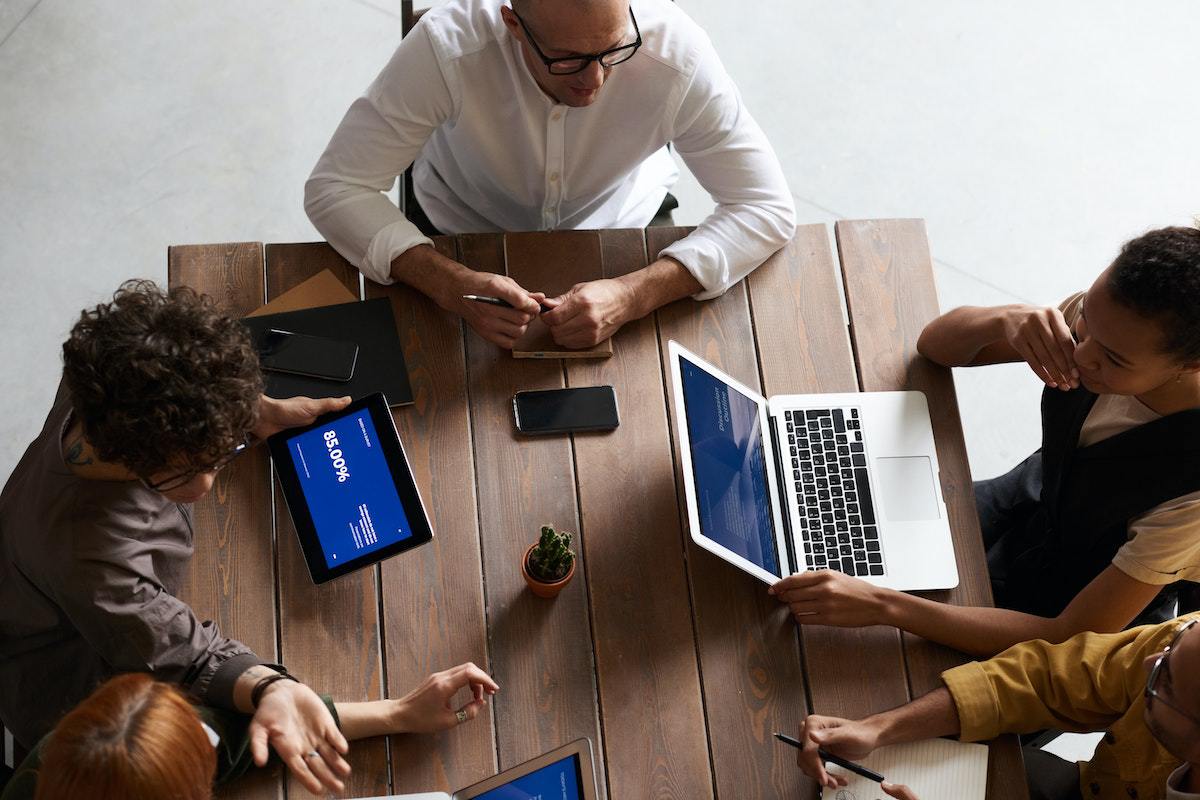 Canvas do marketing digital debatido em reunião ao redor de mesa de madeira em empresa enquanto pessoas usam notebooks e tablets