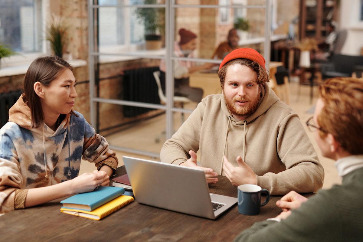 Reunião: Carreira no marketing Pessoas debatendo Carreira no marketing ao redor de mesa em reunião usando notebooks e livros durante a conversa