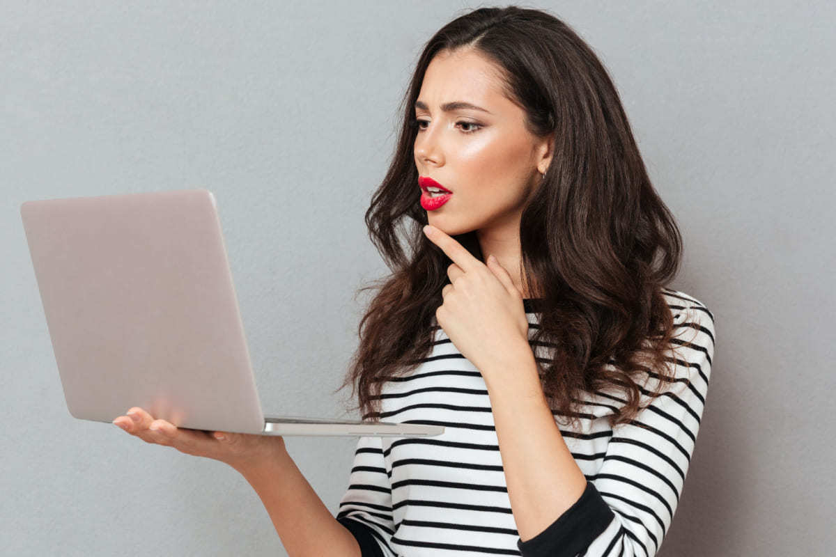 Mulher com notebook na mão direita e mão esquerda no rosto pensativa