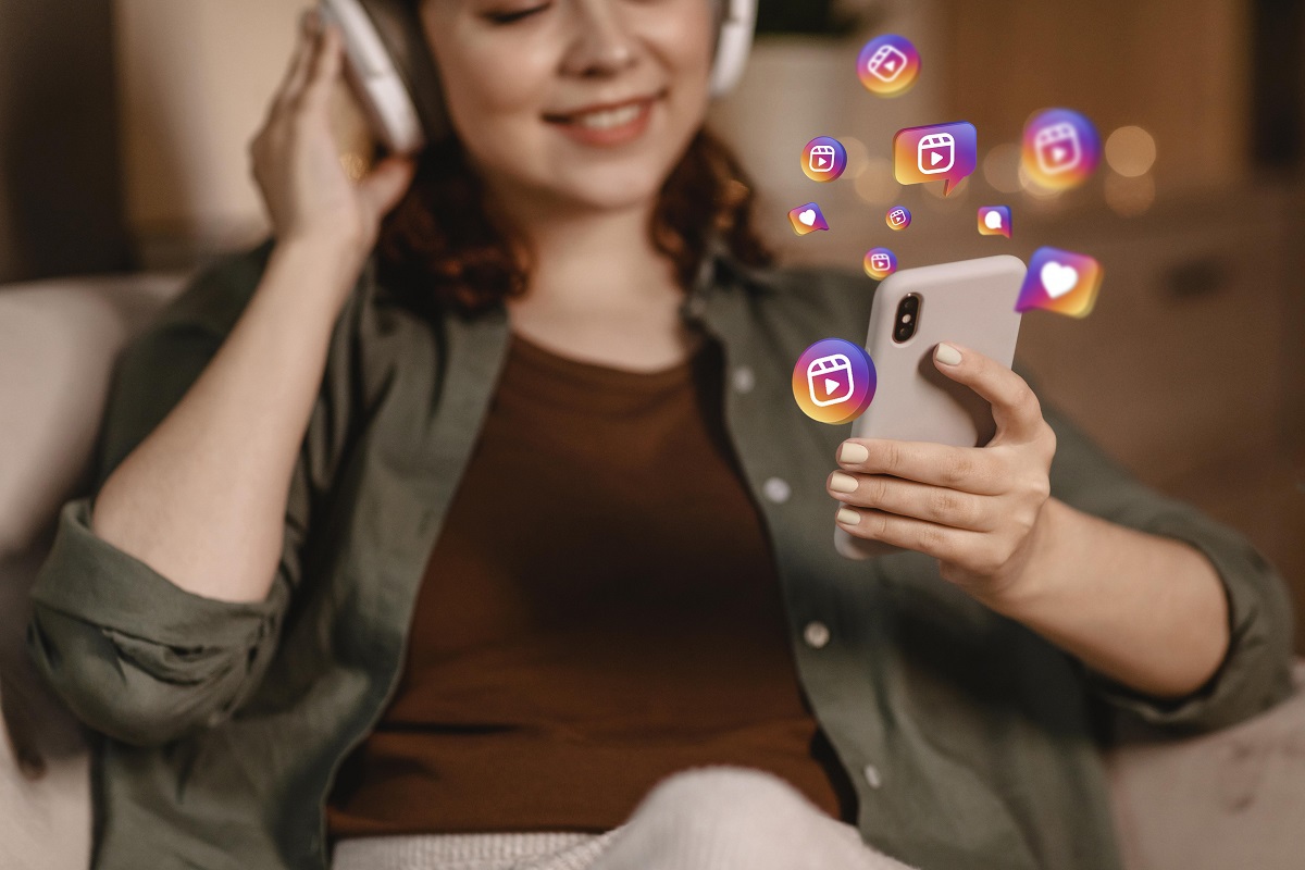 Mulher sentada em poltrona com smartphone nas mãos com símbolos da rede social Instagram saindo do mesmo em montagem e com fone de ouvido sem fio headphone