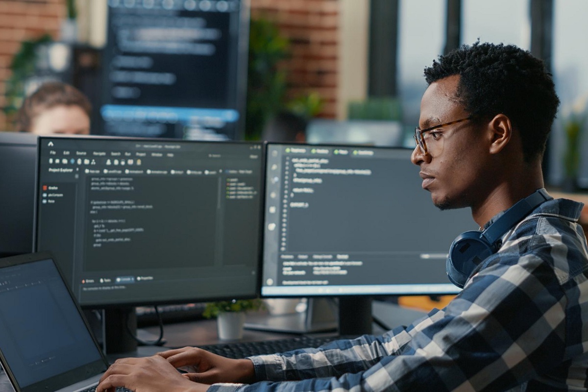 Programador: Data Science Programador usando notebook com mais dois monitores para analisar códigos