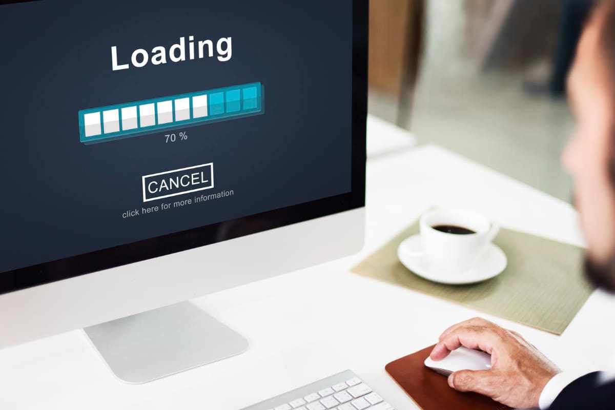 Homem usando computador com tela aberta em Loading carregando algo no seu monitor ao lado de xícara de café cheia