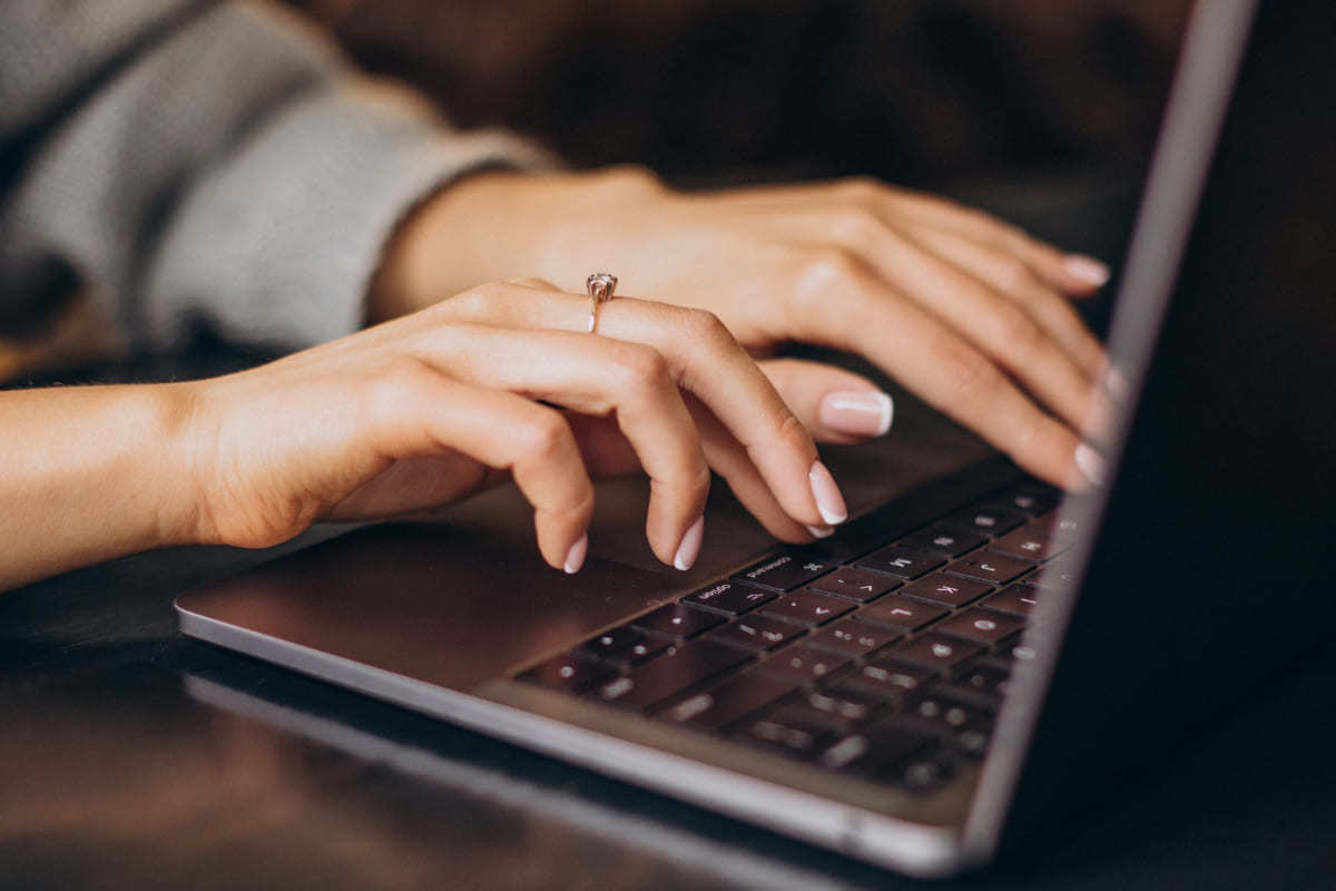 Mulher analisando Embed code em notebook trabalhando em home office com anel no dedo médio da mão direita com pequena pedra e na cor dourada
