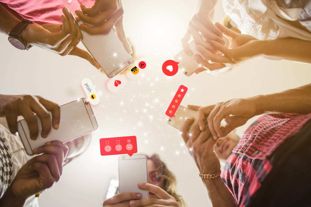 Redes: Ferramentas para criar GIFs Foto tirada de baixo para cima de cinco pessoas com seus celulares nas mãos e símbolos de redes sociais saindo da tela dos mesmos