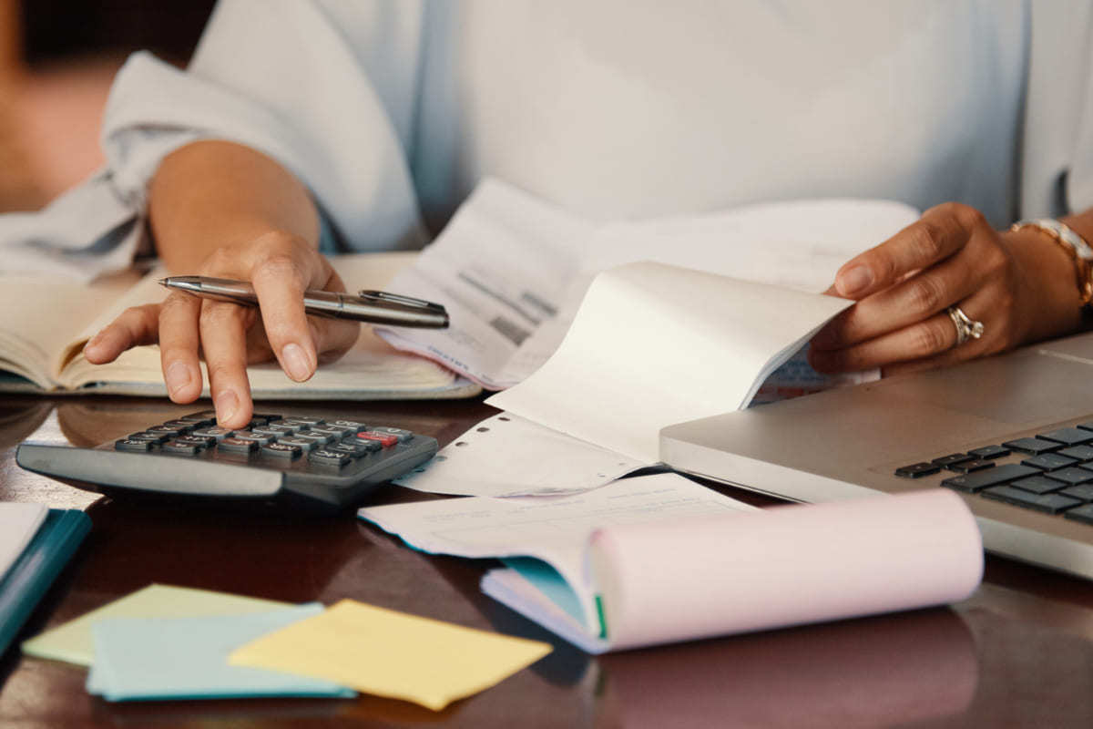 Calculadora: Finanças corporativas e-commerce Homem calculando Finanças corporativas e-commerce com papéis e calculadoras