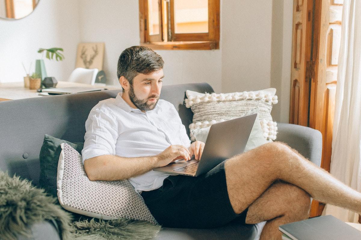 Homem sentado em sofá de casa com notebook no colo trabalhando em Home office e produtividade não comprometida