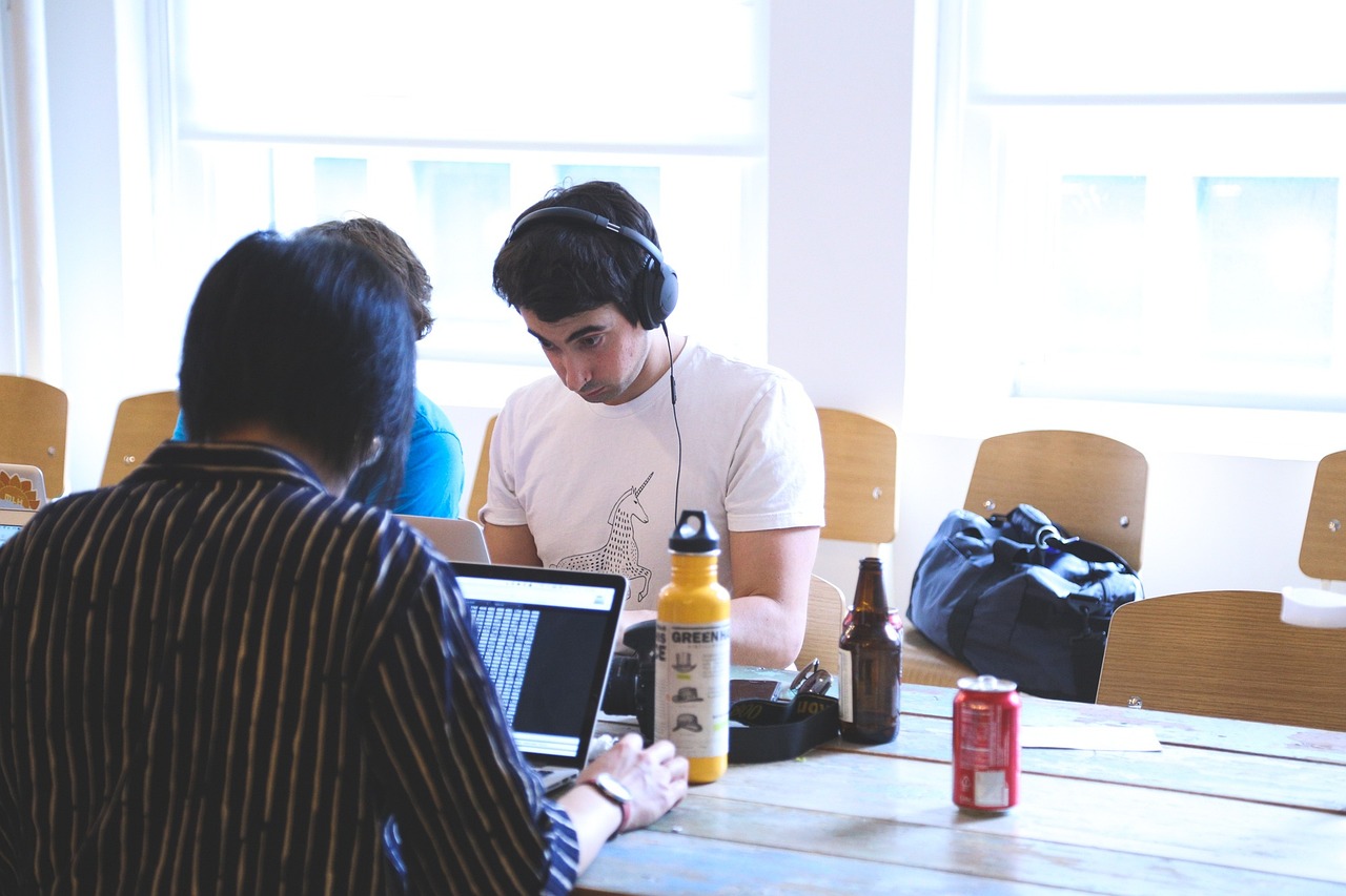 Time reunido e concentrado ao redor de mesa em local de trabalho usando notebooks e headphones