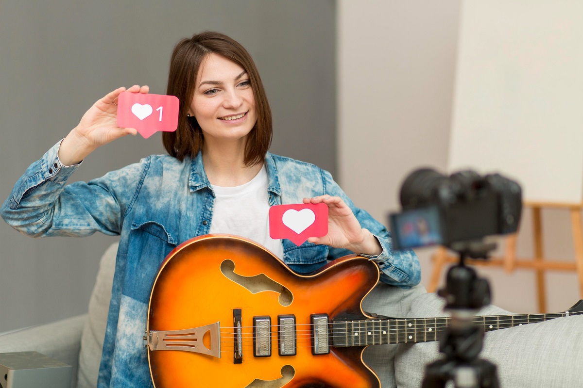 Live no Instagram feita com mulher segurando guitarra em símbolos de like em plaquinhas pequenas diante de câmera enquanto sorri