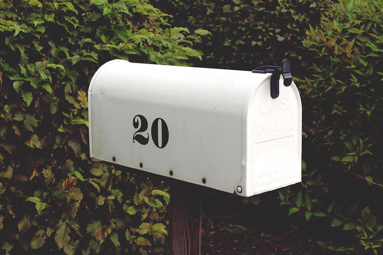 Caixa de correios para depósito de Mala direta na cor branca e com número 20 preto na sua lateral e na frente de plantas similares à arbustos