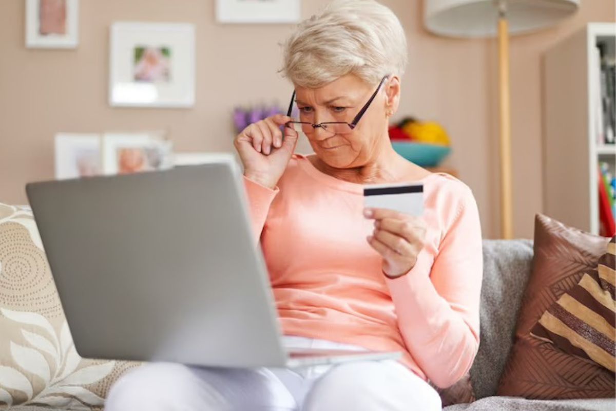 Mulher analisando oferta de Marketing convencional com notebook no colo em sua casa e segurando cartão de crédito nas mãos, enquanto tira óculos do rosto como se tivesse incrédula com o que vê