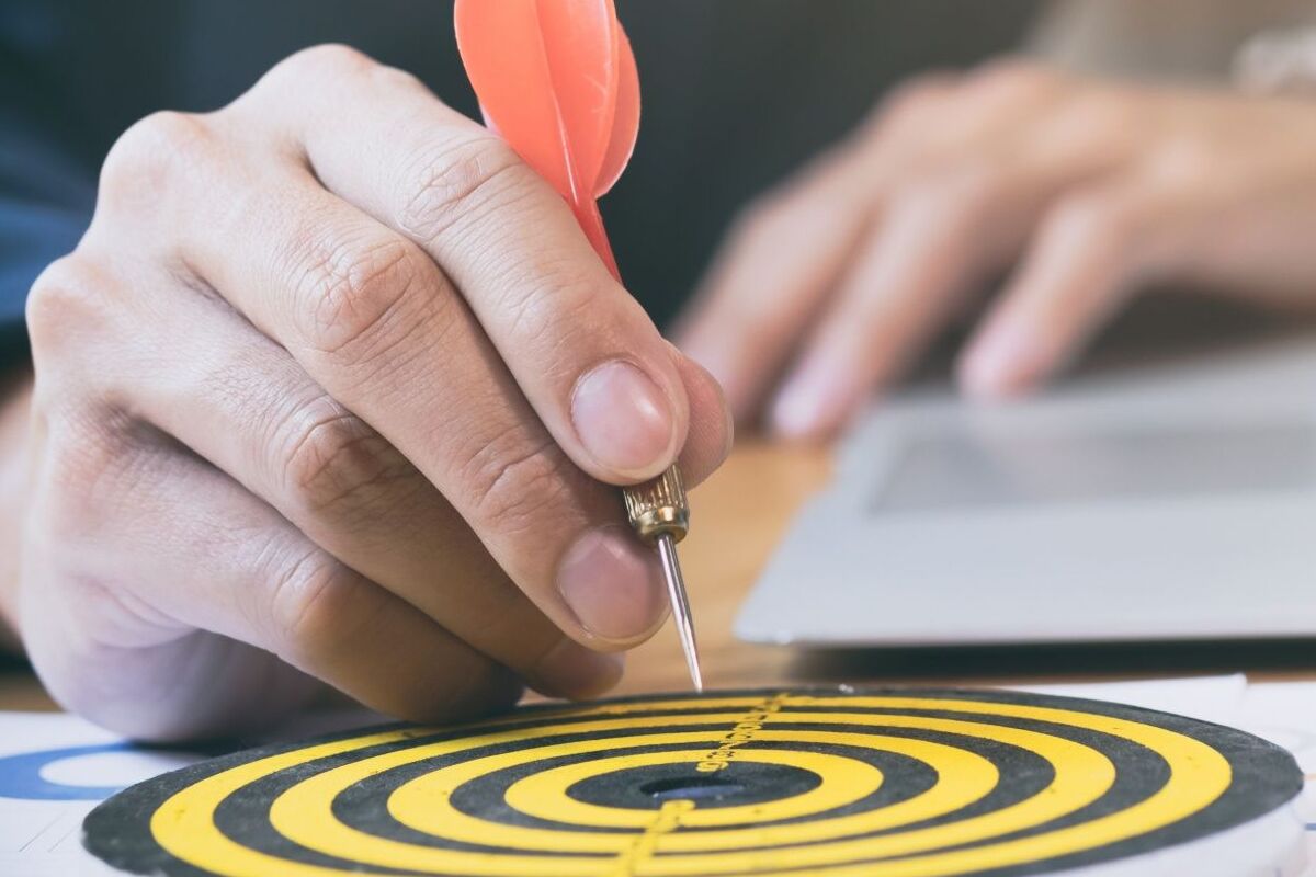 Alvo: Matriz Ansoff Pessoa segurando dardo e fixando o mesmo no centro de alvo de papel nas cores amarelo e preto