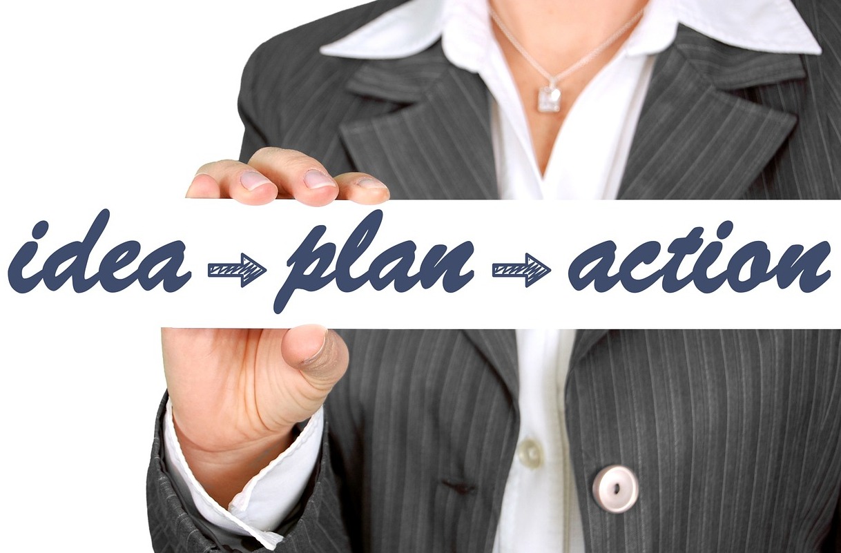 Planejamento: Métricas de negócio Pessoa segurando plaquinha de planejamento para análise de Métricas de negócio onde contém, em inglês, as palavras Ideia, Plano e Ação com uma seta ligando uma palavra à próxima