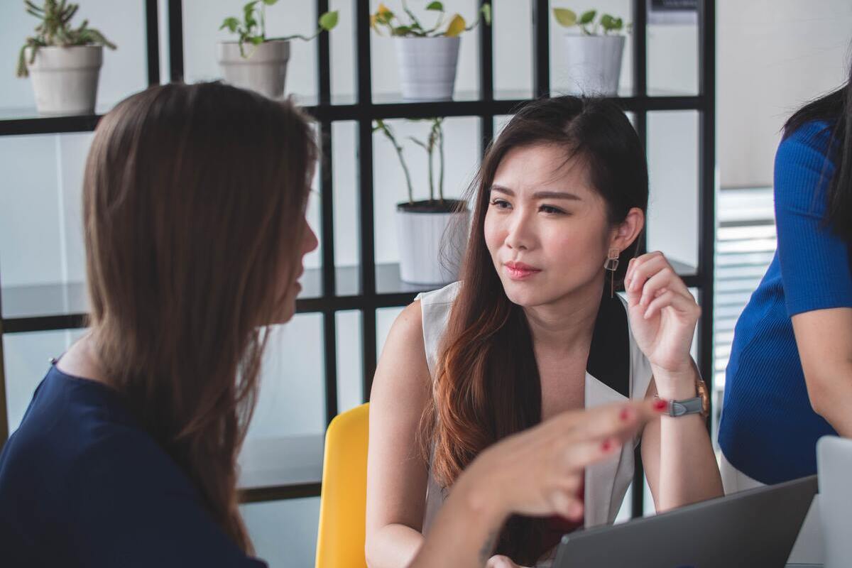 Trabalho: Negociação Mulheres durante Negociação em local de trabalho conversando ao redor de colegas e diante de notebook cinza sobre mesa