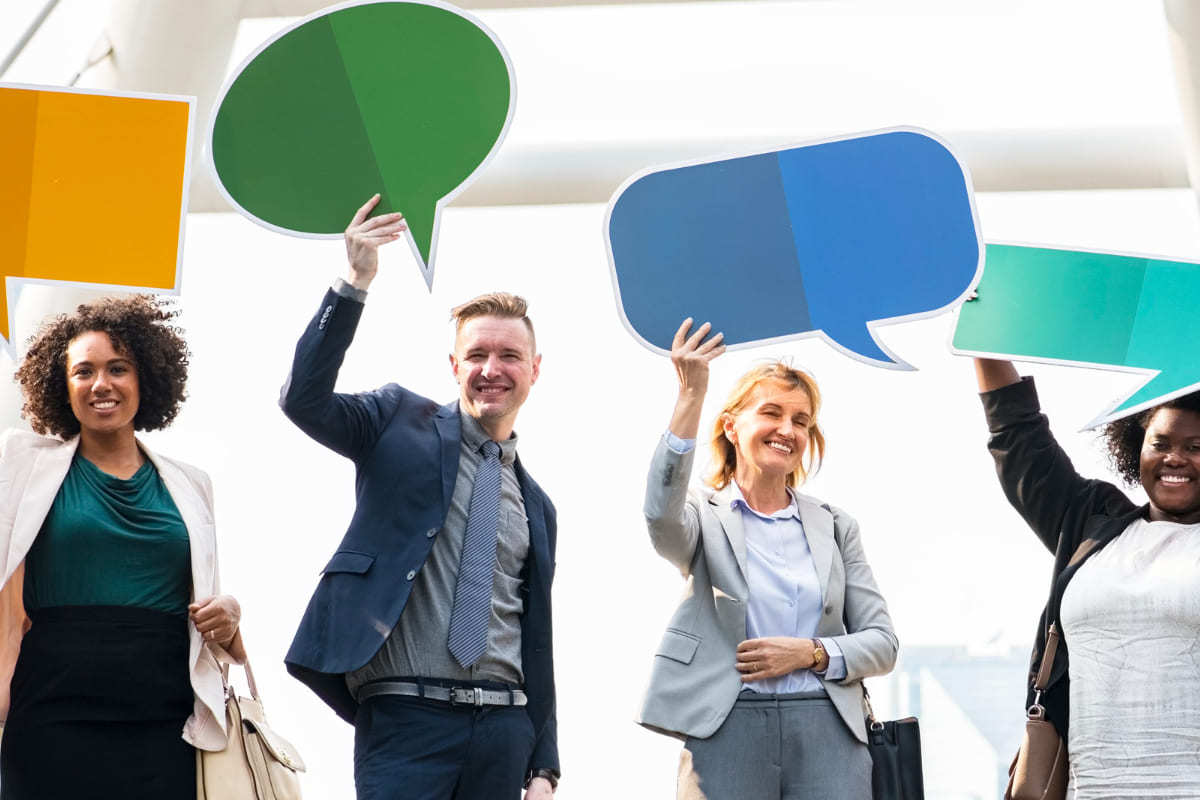 Homens e mulheres sorridentes usando roupas sociais com blazer segurando plaquinhas que simulam símbolos web para conversação via mensagem de texto em apps ou sms