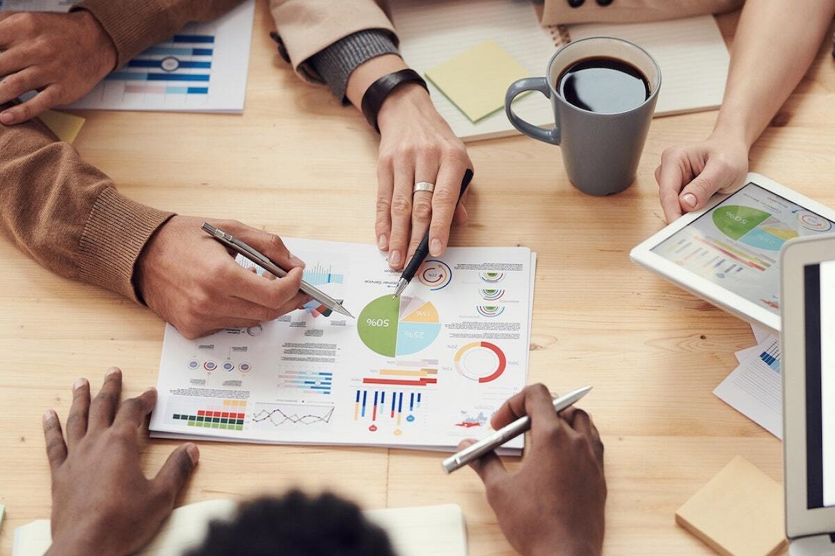 Reunião: Plano de negócios Pessoas em reunião debatendo sobre gráficos e dados em folhas impressas referentes à Plano de negócios de marca ao redor de mesa de madeira