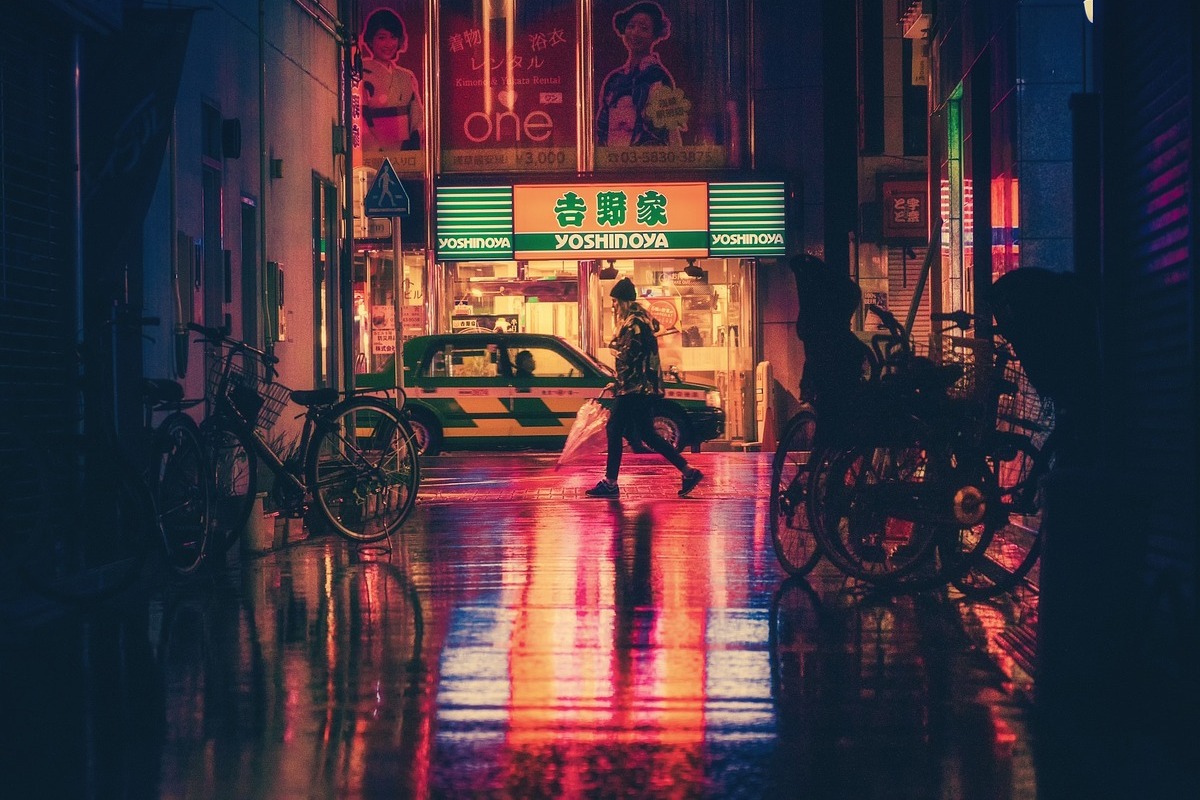 Placa: Preset Pequena viela que termina em frente à pequena loja com placa com inscrições em línguas orientais e nome yoshinoya e pessoa passando em frente à loja e táxi parado na rua
