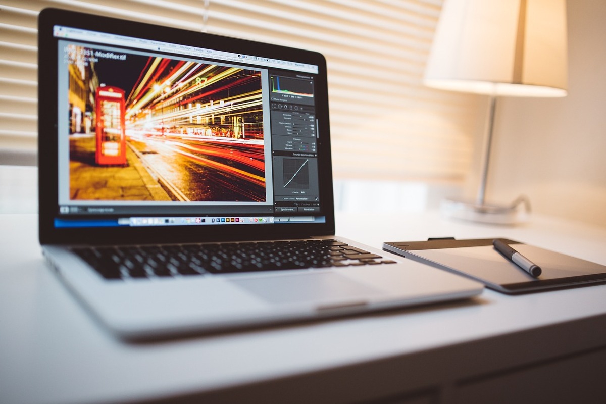 Notebook: Preset Notebook sobre mesa branca ao lado de agenda e caneta sobre a mesma e com abajur ao fundo em desfoco e foto dos mesmos objetos na tela do aparelho para usar o Preset em Home office