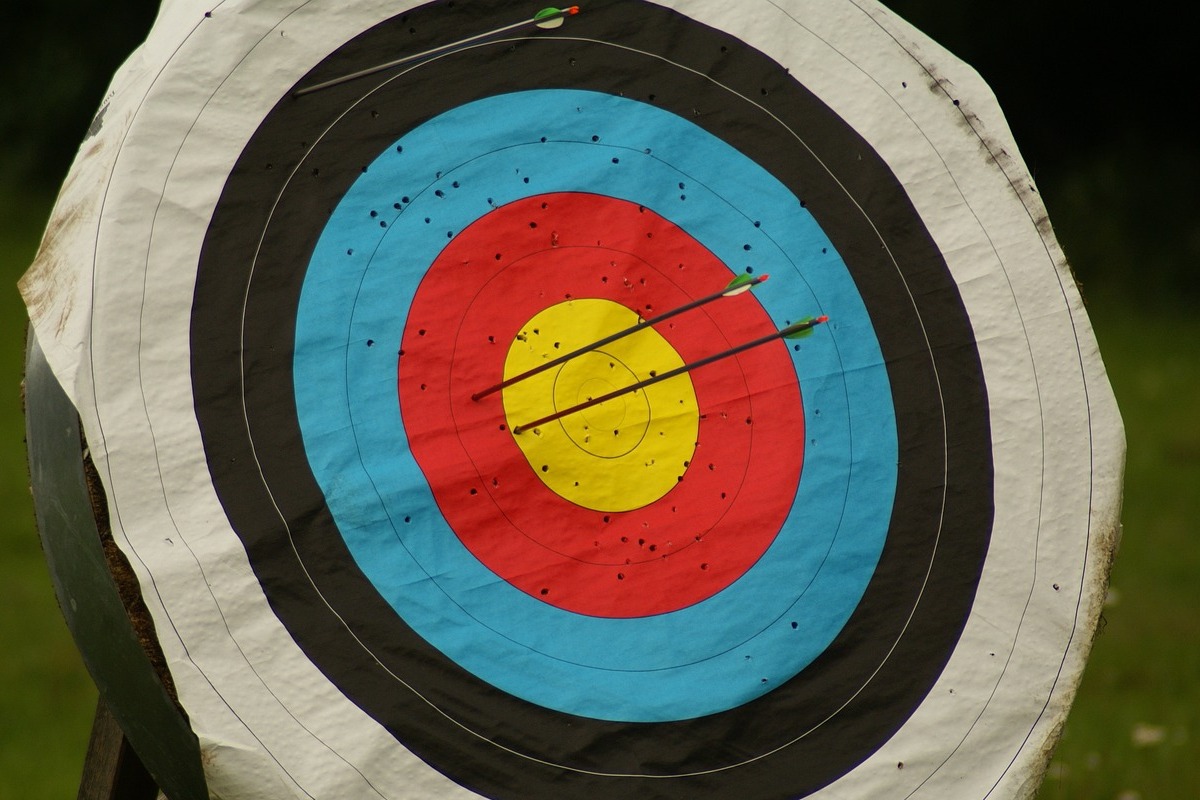 Foto de flechas atingindo centro de alvo de madeira com cores branco, preto, azul, vermelho e amarelo no meio