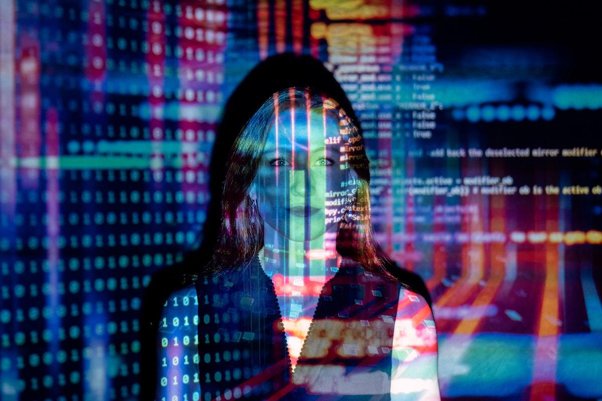 Montagem com mulher de pé parada diante de imagem com código binário e código de programação de sistema em forma de holograma representando Profissões do futuro