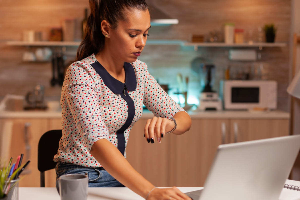 Mulher usando notebook sobre mesa na cozinha de sua casa