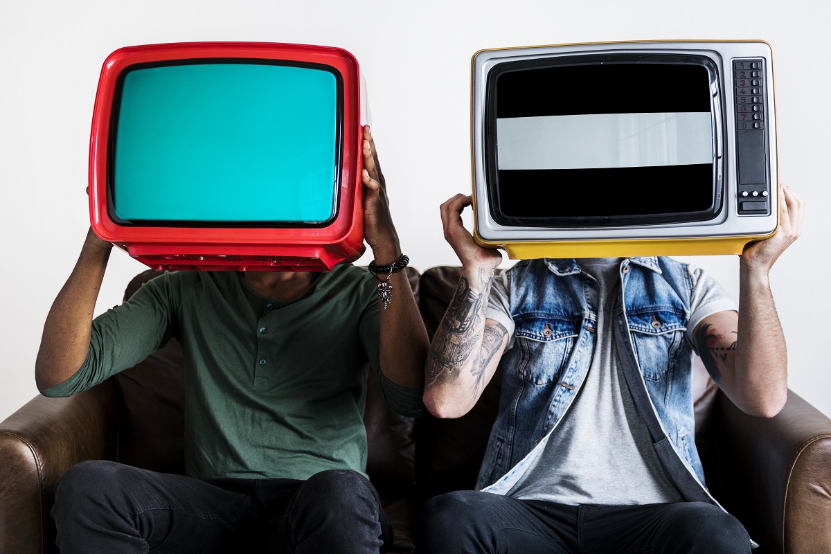 Pessoas sentadas em sofá segurando televisões antigas diante de suas cabeças para foto representando o termo Transmídia