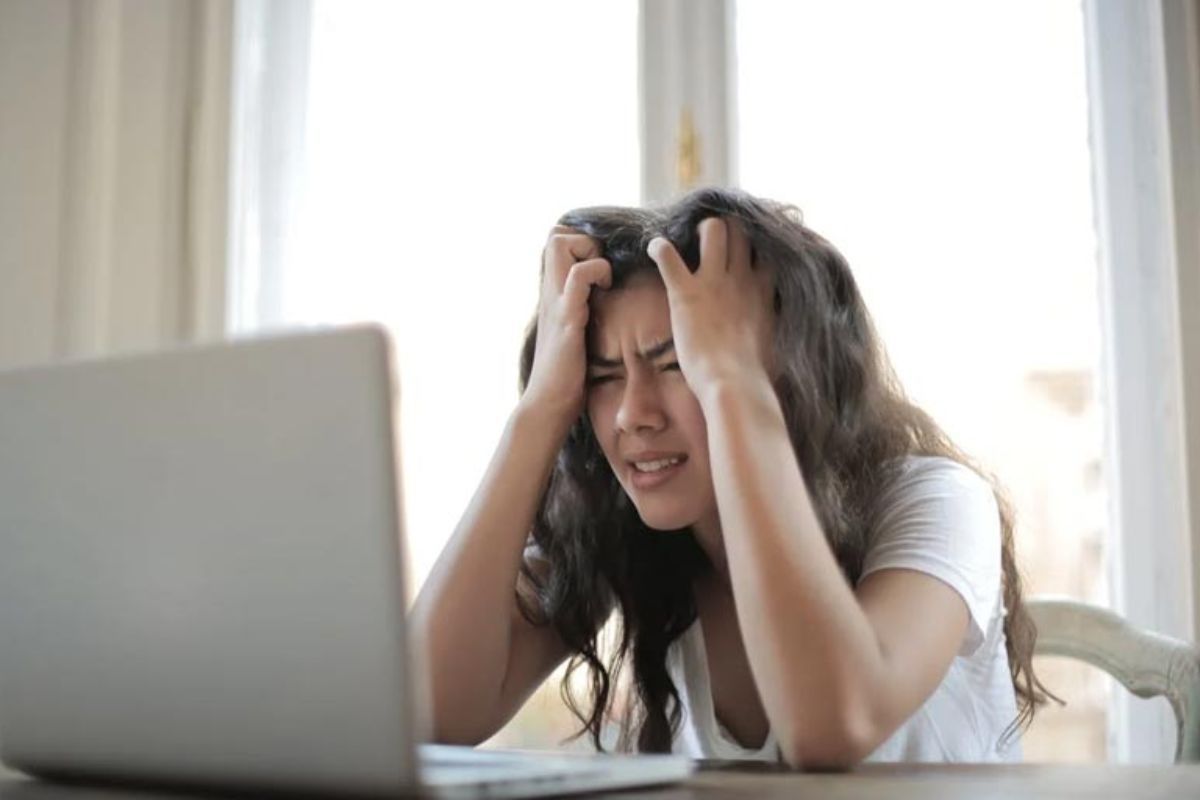 mulher cansada com mãos na cabeça, olhando para o notebook