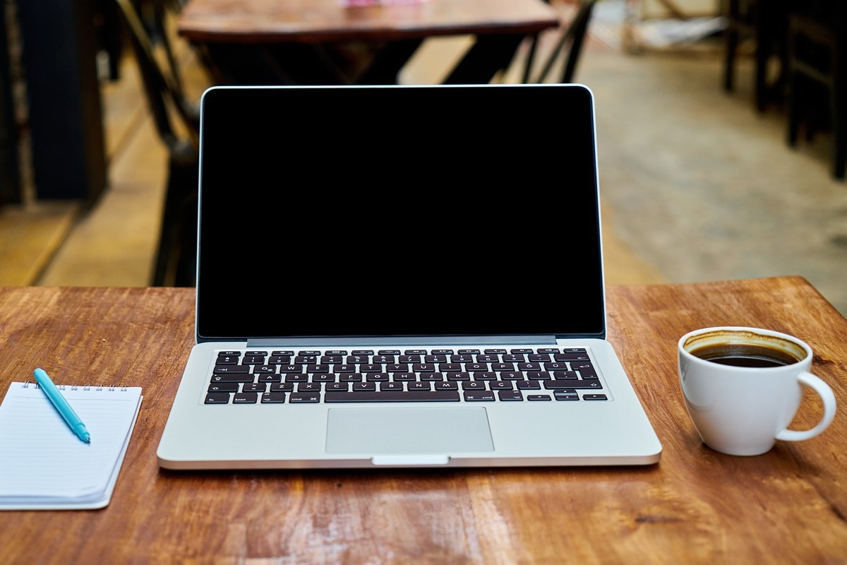 laptop em cima de uma mesa, do lado de uma xícara de café
