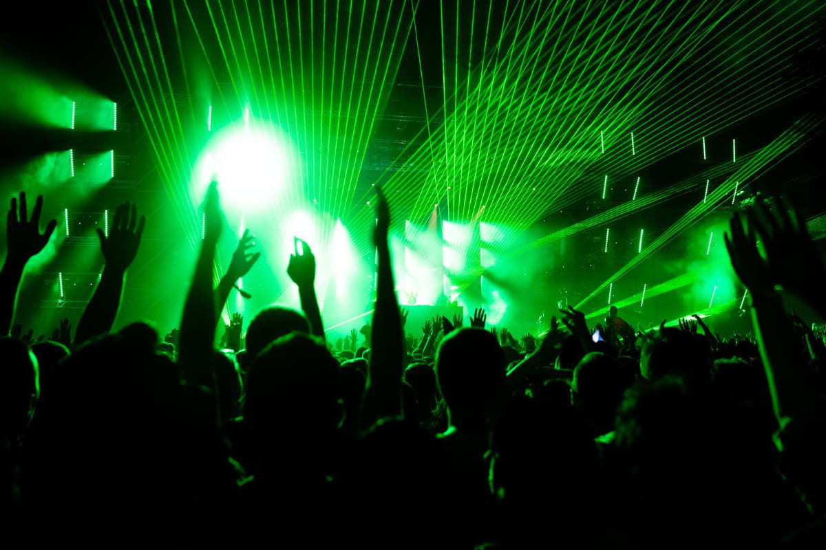 Show com palco emitindo luzes verdes e pessoas jogando mãos aos céus se divertindo em local que usou Marketing para eventos