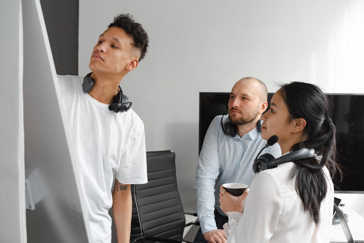 Mulher e dois homens da mesma equipe de empresa criando Roadmap enquanto anotam algo em local que não está visível na foto