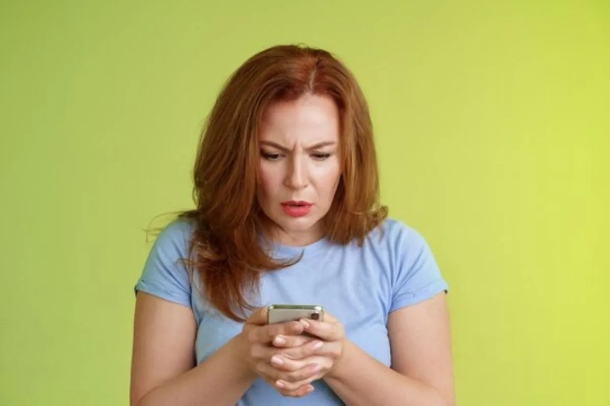 Como usar o FOMO nas suas estratégias de marketing? Mulher olhando para o smartphone com expressão de preocupação, sugerindo ansiedade ou FOMO (Fear of Missing Out).