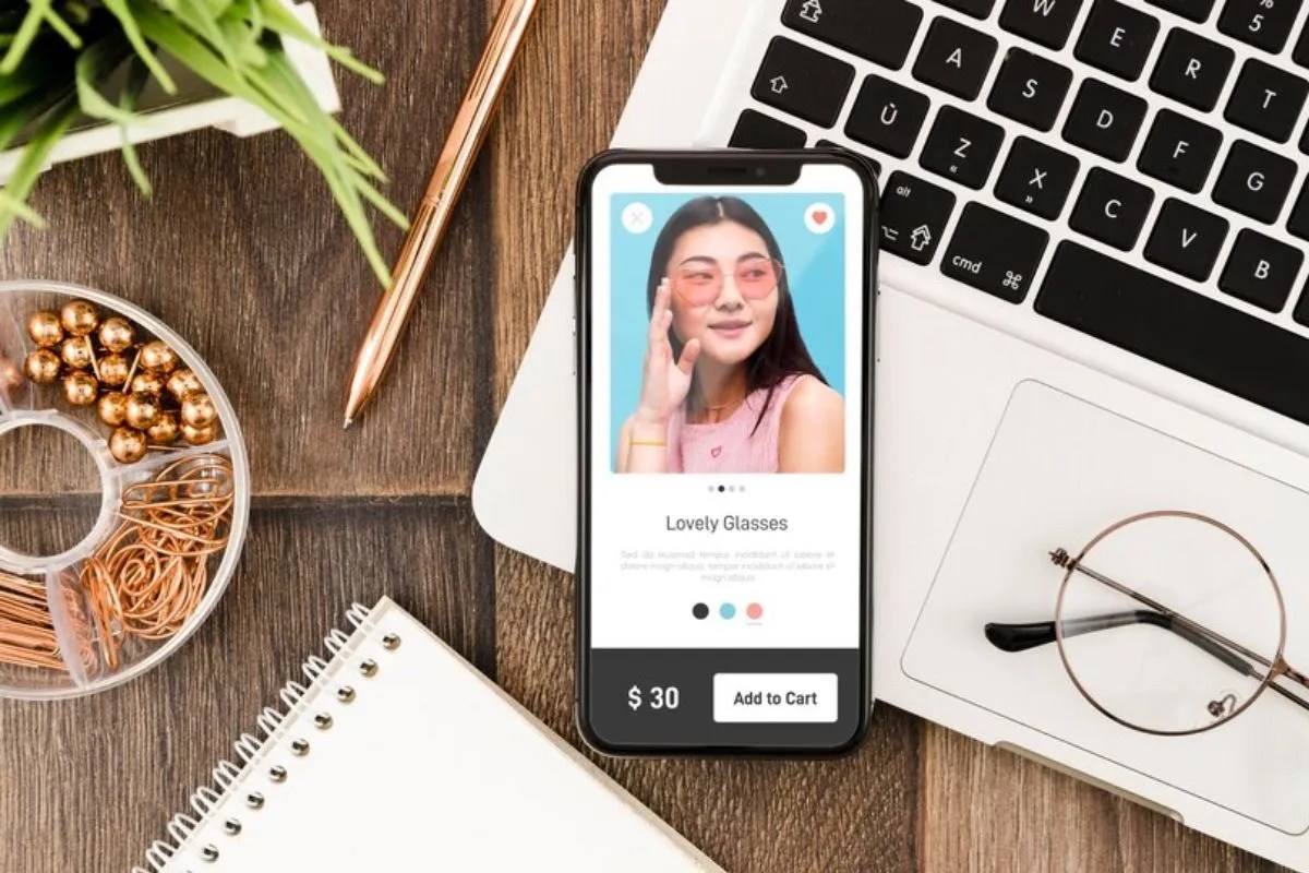 Link na Bio do Instagram: passo a passo para criar, editar e incrementar seu perfil Tela de smartphone exibindo uma loja online com óculos, ao lado de um laptop, caderno e acessórios de escritório.