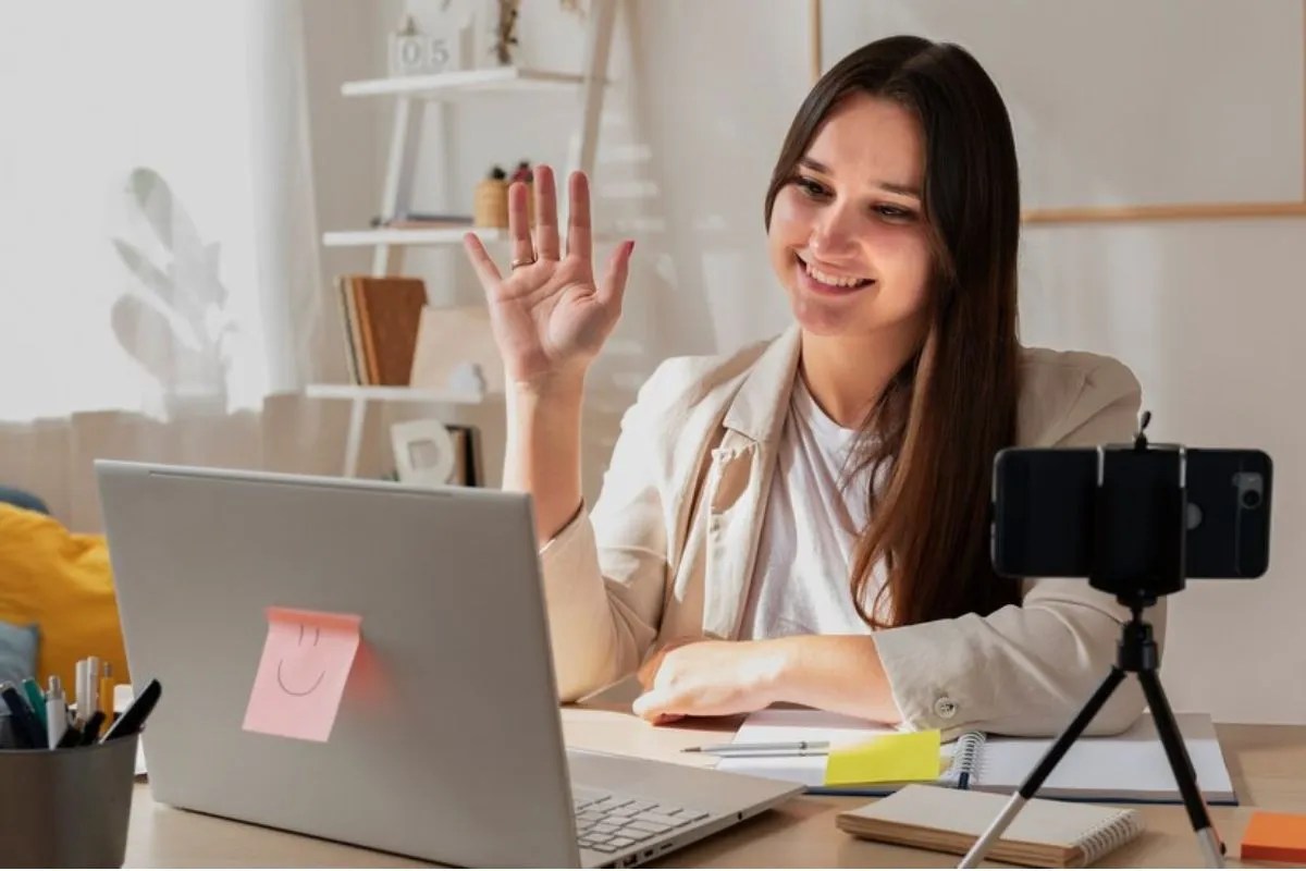O que é UGC (conteúdo gerado pelo usuário) e qual é o seu poder em estratégias de marca? Mulher sorridente acenando durante uma videochamada em casa