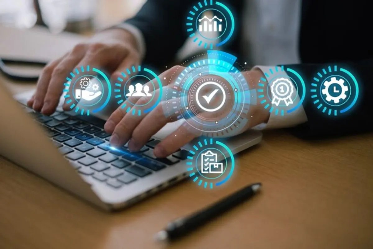 O que é o ClickUp e como ele pode otimizar a gestão de projetos? Pessoa de roupa social com blazer digitando em notebook sobre mesa de madeira com caneta preta ao lado e imagens holográficas com símbolos visuais em montagem digital.