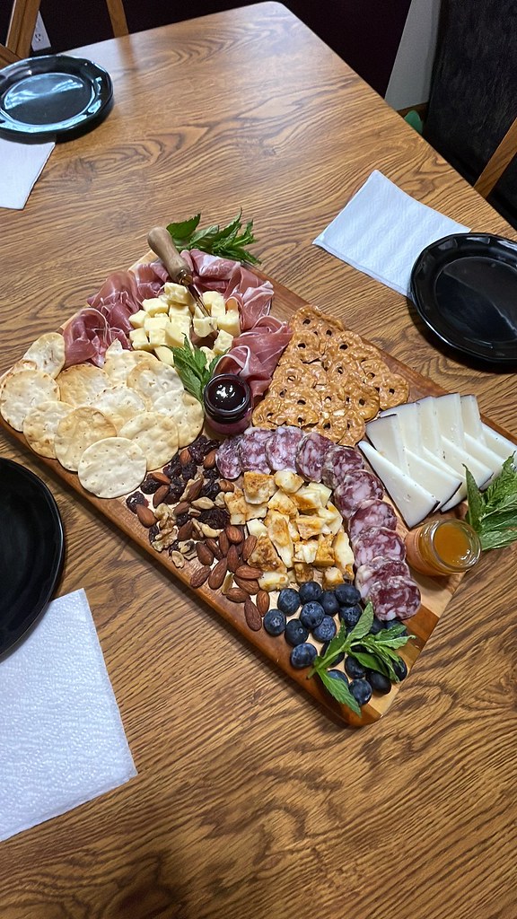My absolutely bomb charcuterie board laying in the middle of the table, surrounded by three small black plates that each have a paper napkin beside them. I'm going to give the details of the board in the next photo, don't worry.