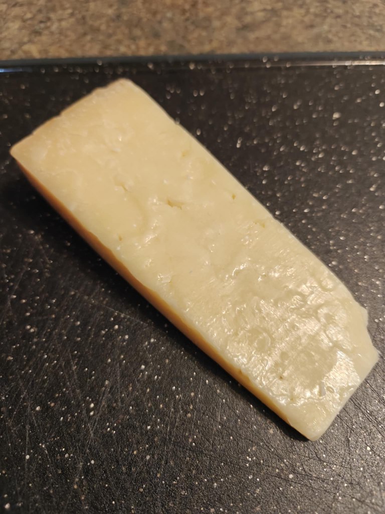 A triangular hunk of cheddar, off white in color and resting on a black cutting board.