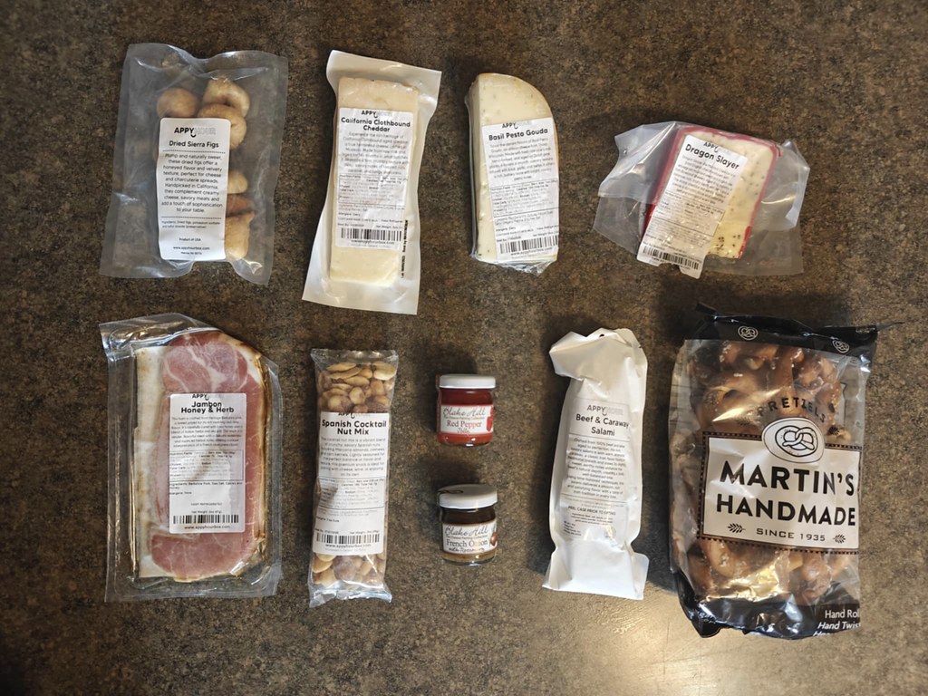 Everything I got from the box laid out in two rows on the counter. Everything is still in its packages so it's kind of hard to see everything, but there's three cheeses, two meats, a bag of pretzels, two little spread jars, a bag of nuts, and a bag of figs.