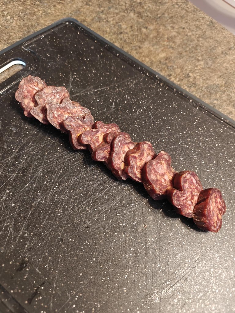A log of salami that has been sliced into equal sized rounds and is laying out on a black cutting board. 