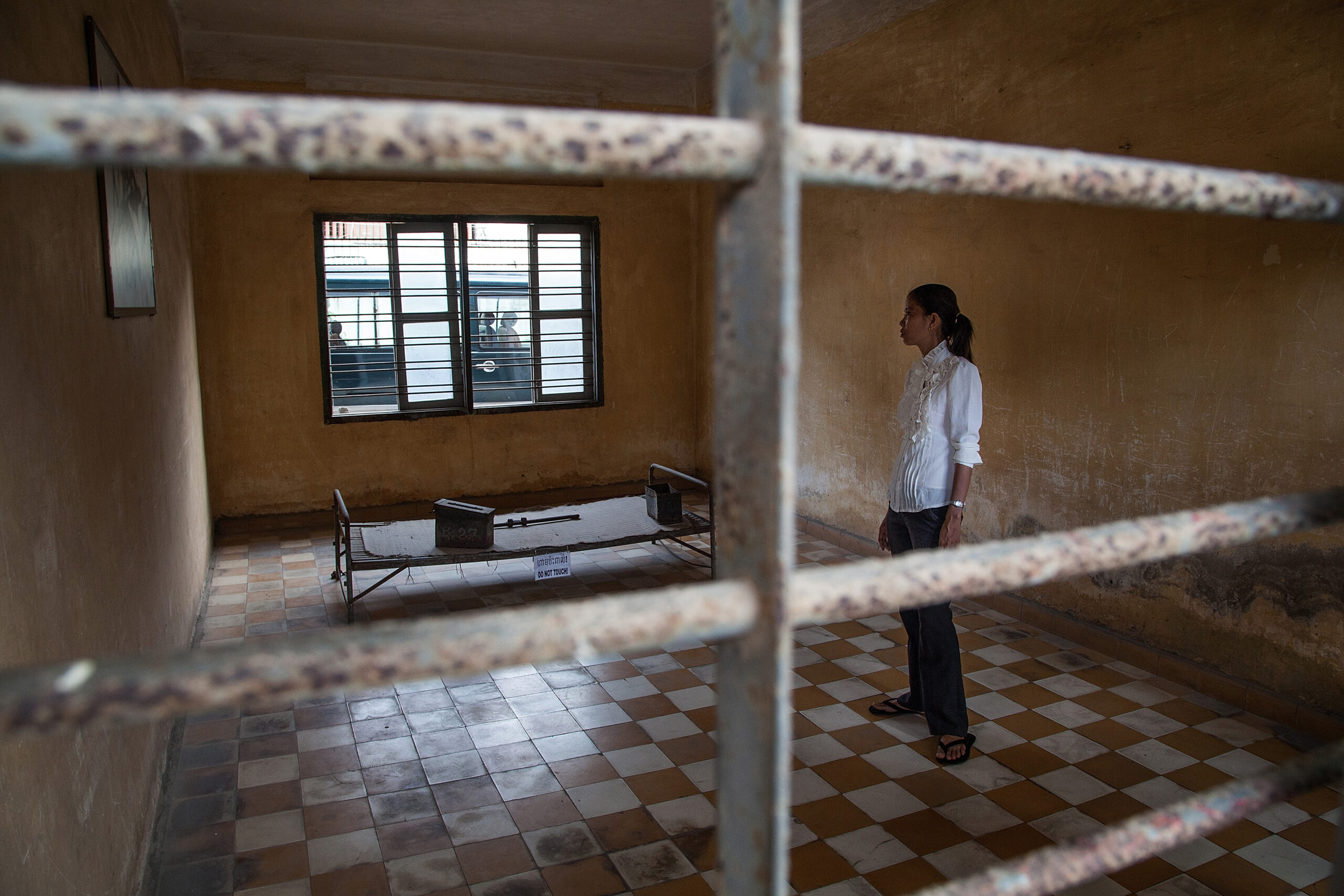 A young Cambodian woman stands in one of the torture rooms of Tuol Sleng prison.