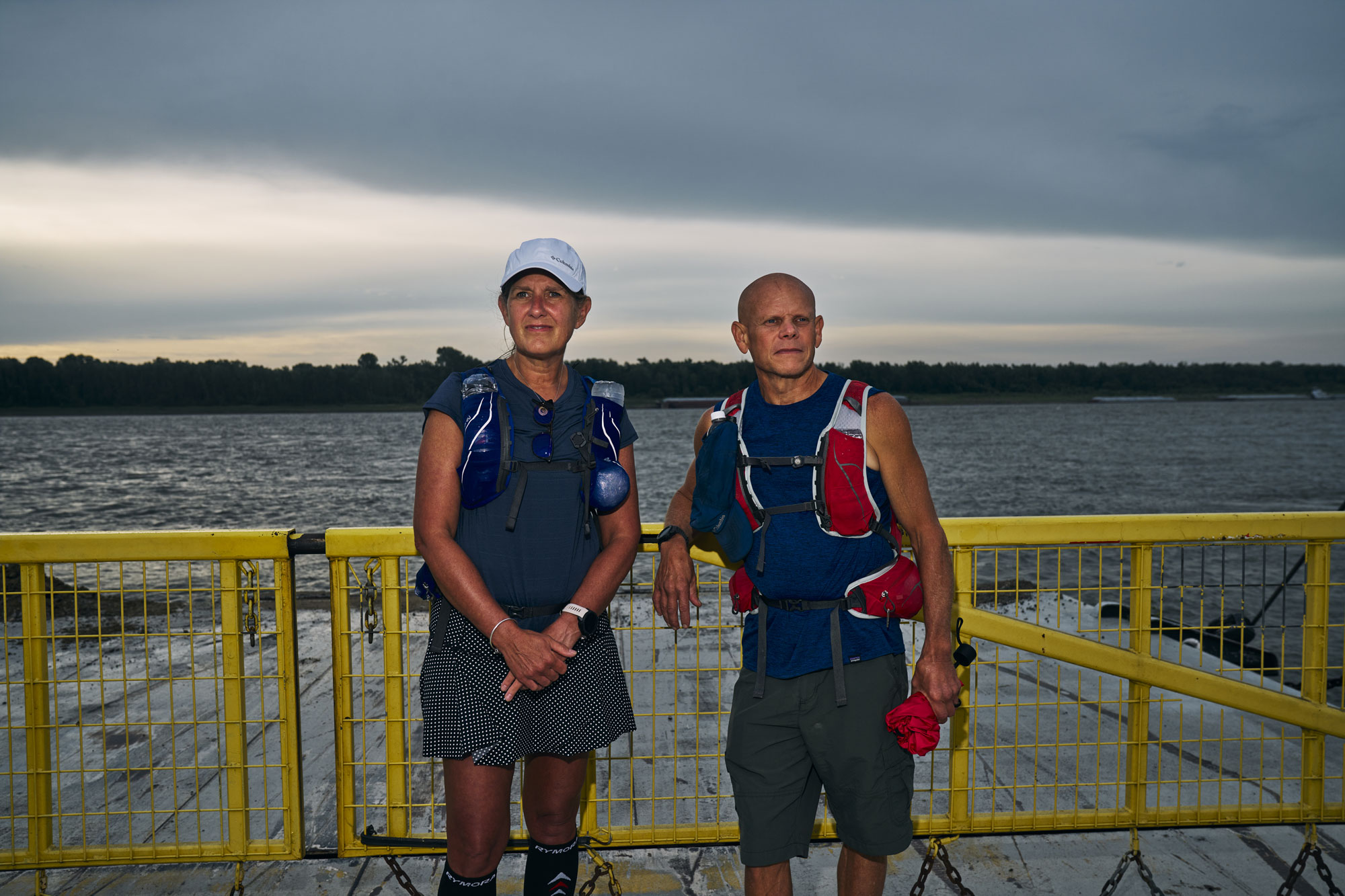 Allison and Todd Barcelona lean against the rail of a ferry on the Mississippi River, the wake trailing behind the boat.